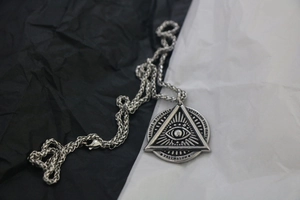Detailed close-up of retro silver Freemason triangle eye pendant on steel chain