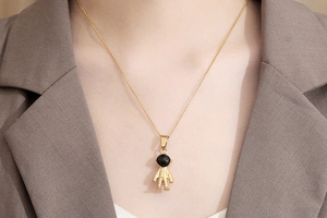 Close-up of a gold astronaut pendant necklace with black enamel detail on model