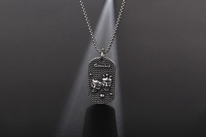 Makrodetail des Zwillinge-Anhängers in Vintage-Silber mit geprägtem Maskenmuster