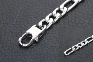 Macro shot of silver Figaro chain bracelet with lobster clasp on black leather