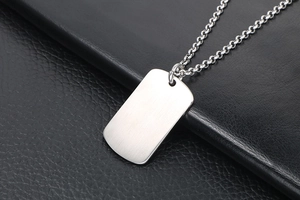 Macro detail of brushed stainless steel dog tag pendant on a textured black leather surface