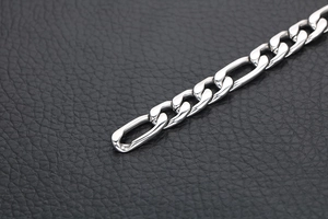 Macro shot of polished silver Figaro chain bracelet on a black leather background