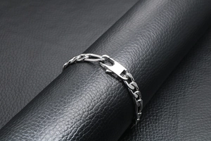 Macro view of silver flat curb chain bracelet with modern buckle on black leather background