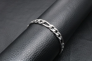 Polished silver Figaro chain bracelet for men displayed on black leather textured surface