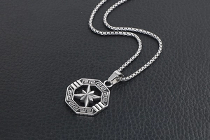 Detailed close-up of retro silver compass pendant with greek key border on box chain