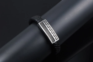 Détail du bracelet en cuir tressé noir avec motif grec sur plaque en acier inoxydable