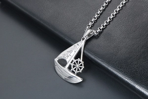 Macro detail of silver sailboat pendant featuring a rudder and smooth metal texture