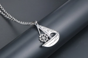 Macro shot of silver sailboat pendant with rudder detail and smooth chain