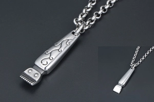 Close-up of silver hair clipper pendant with engraved floral vine patterns on a chain