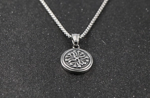 Macro view of silver stainless steel round pendant with radial wave pattern and box chain