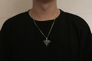 Detailed view of gothic shield pendant with green gemstone on bicolor chain for men