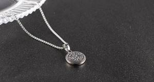 Close-up of stainless steel necklace with embossed sun pattern round pendant on black surface