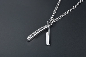 Detailed macro of folding razor pendant with vintage floral engraving and mirror finish