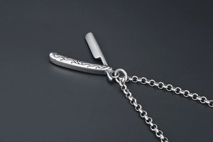 Detailed view of a vintage stainless steel folding straight razor pendant with ornate carving