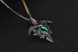 Macro detail of gothic eagle wing pendant with green cat eye stone and mixed tone chain