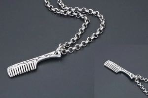 Macro view of a stainless steel comb pendant with vintage floral engravings and rolo chain