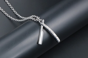 Detailed macro of a silver barber razor pendant with intricate vintage floral carvings