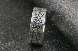 Gros plan d'une bague en acier titane avec gravure toile d'araignée noire polie