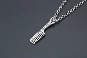 Macro view of stainless steel comb pendant with intricate scrollwork on cross chain