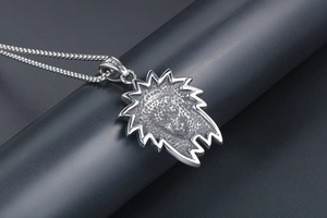 Detailed shot of a silver lion head pendant on a round bead chain over grey cylinder