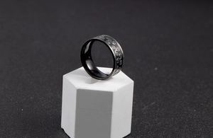 Macro view of black stainless steel triskelion ring on a white hexagonal display stand