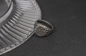 Close-up of vintage oxidized stainless steel ring with crater texture and center symbol