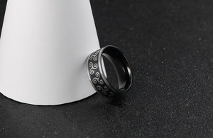 Detail of black stainless steel ring featuring etched silver triskele patterns on the band