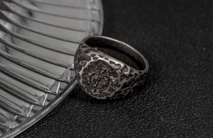 Macro detail of men's vintage steel ring with rugged distressed texture and engraved crest