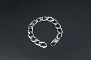 Gros plan d'un bracelet gourmette argenté avec un grand fermoir mousqueton sur fond noir