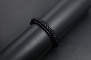 Détail d'un bracelet en cuir tressé noir présenté sur un support cylindrique