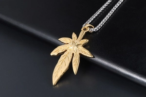Gros plan du pendentif feuille dorée avec nervures fines sur une chaîne en métal tressé argent