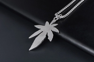 Détail du pendentif feuille d'érable en acier brossé sur fond de cuir noir texturé
