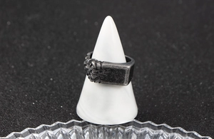 Macro detail of dark grey vintage stainless steel ring with woven texture on marble stand