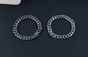 Detailed view of two gunmetal stainless steel cuban link bracelets on black leather