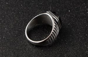Gros plan d'une bague en acier pour homme avec une pierre noire et des reliefs ciselés