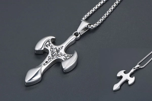Detail of silver cross pendant featuring intricate black vintage carvings on stainless steel