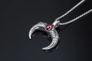 Macro view of silver engraved bull horn pendant with central red gemstone and square link chain