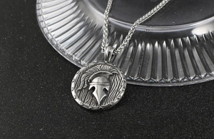 Détail macro du pendentif casque spartiate vintage avec chaîne épi sur fond texturé noir