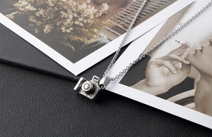 Macro detail of silver camera pendant on black leather with fine cross chain