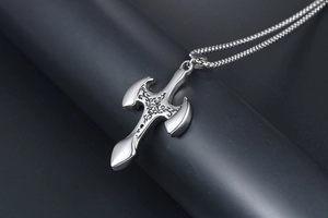 Macro detail of gothic cross pendant with intricate black vine patterns and wheat chain
