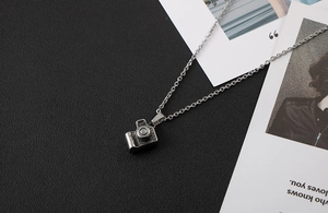 Macro detail of silver camera pendant necklace showing vintage texture on black leather