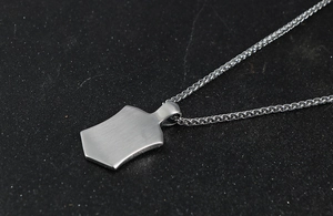 Close-up of brushed silver unicorn shield pendant on a detailed wheat chain necklace