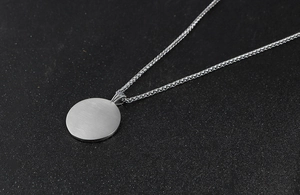 Détail macro du pendentif rond en acier titane argenté avec finition en métal brossé