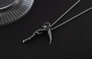 Detail of gothic grim reaper pendant with scythe in vintage silver finish on black surface