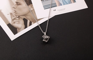 Detailed close-up of a silver vintage camera pendant necklace on black textured leather