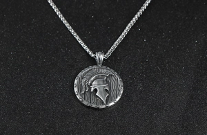 Détail d'un pendentif bouclier avec casque spartiate vintage et sa chaîne en maille épi