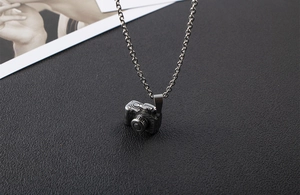 Close-up of vintage camera pendant necklace with detailed lens and buttons on black texture