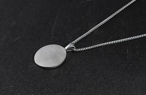 Détail macro du pendentif ovale argenté avec fini brossé et chaîne en blé