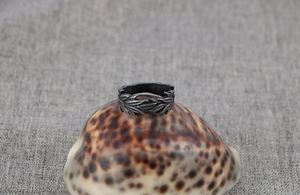 Detail of vintage oxidized steel ring with intricate leaf pattern on textured seashell