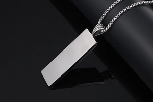 Macro view of silver rectangular pendant showing brushed metal texture and engraved bail